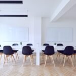 Salle de réunion avec table blanche, chaises noires, deux tableaux blancs et télévision