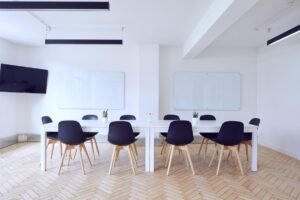 Salle de réunion avec table blanche, chaises noires, deux tableaux blancs et télévision